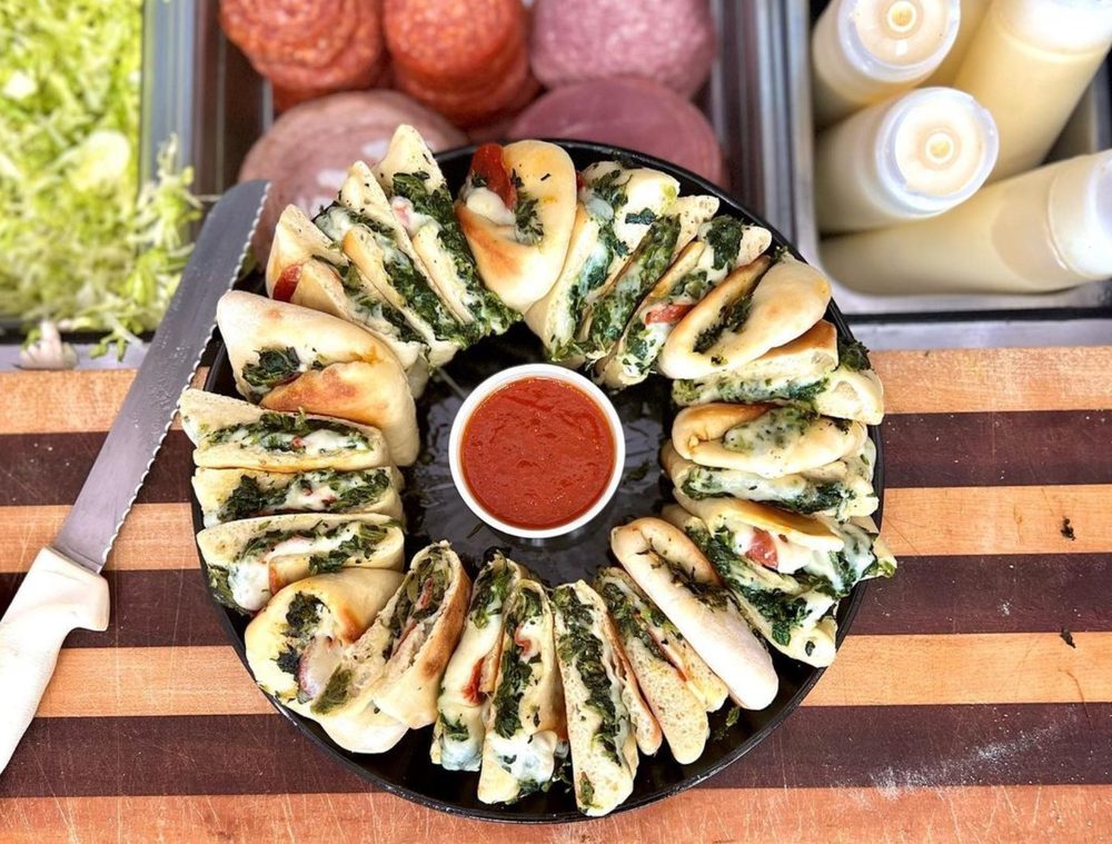 Catering pie platter with spinach pies arranged in a ring around a cup of marinara sauce on a round black tray